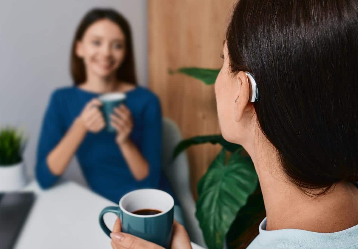 adult woman with hearing aid having coffee with friend